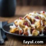 Side view of a generous portion of slow cooker French toast casserole, rich with cranberries and apples, served on a black plate on a rustic wooden surface, accompanied by a black napkin and silverware.