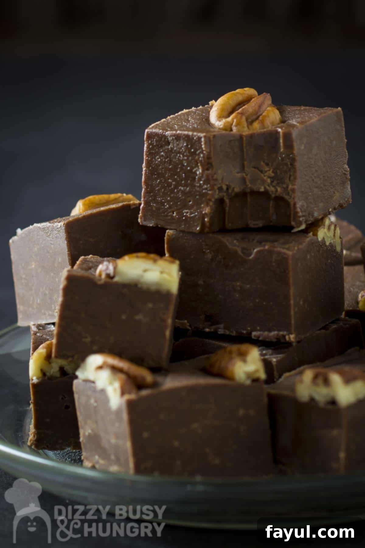 Side close up shot of multiple pieces of fudge stacked on each other on a clear plate with a black background, garnished with a sprinkle of pumpkin pie spice.