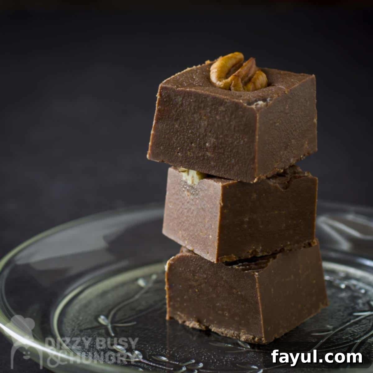 Side close up shot of three pieces of pumpkin spice fudge stacked on a clear plate with a black background, inviting and perfectly set.