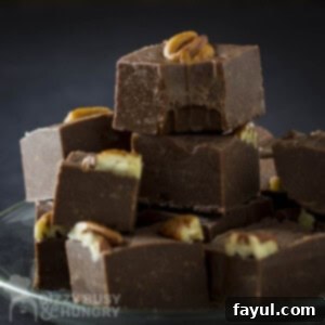 Side shot of multiple pieces of fudge stacked on each other on a clear plate with a black background.