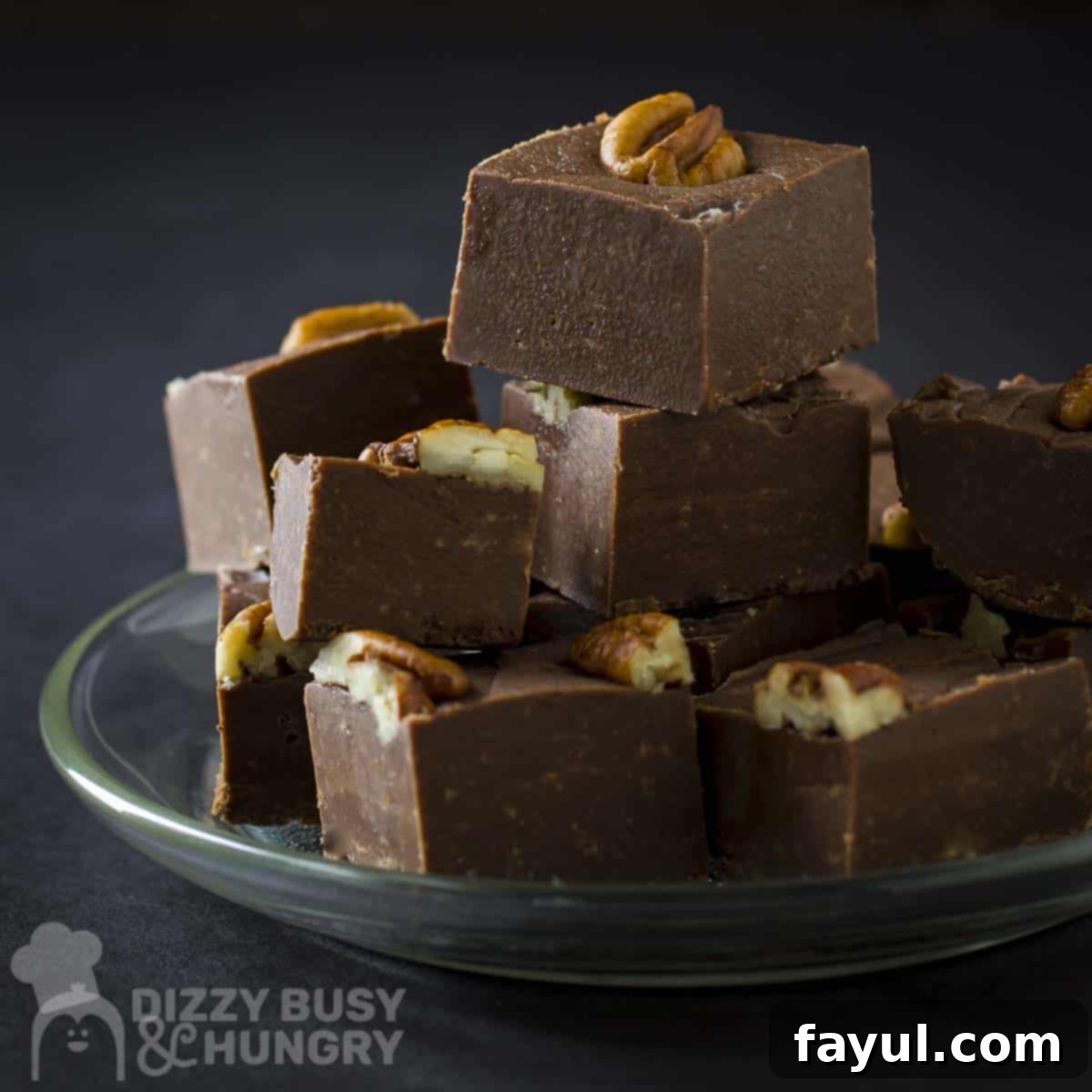 Side shot of multiple pieces of fudge stacked on each other on a clear plate with a black background, with a rich, inviting texture.