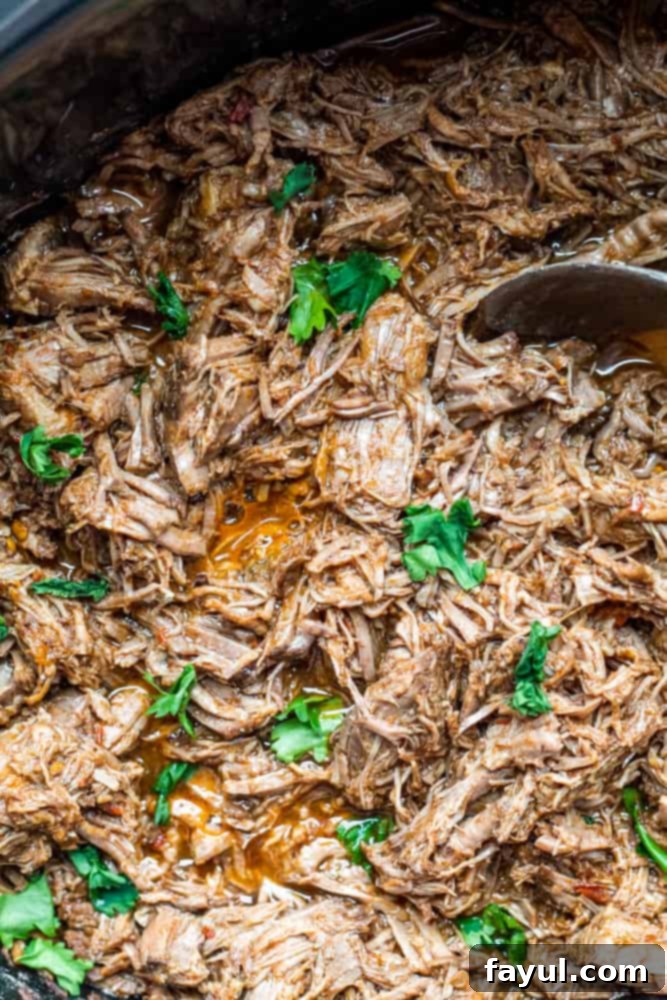 Slow Cooker Mexican Beef Barbacoa 5 Overhead shot of cooked beef in a crockpot with wooden spoon.