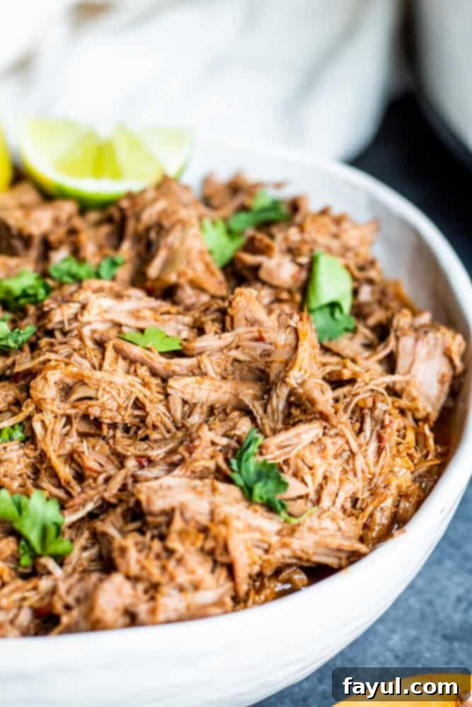 Slow Cooker Mexican Beef Barbacoa 6 Angle shot of beef in a white bowl with cilantro and lime on top.
