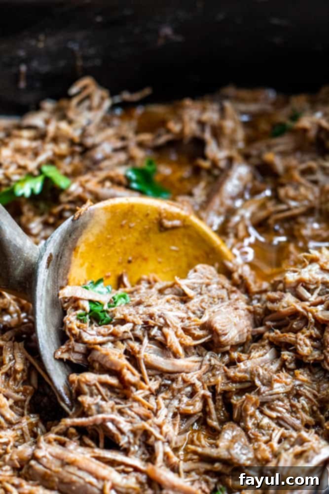 Slow Cooker Mexican Beef Barbacoa 7 Wooden spoon scooping up beef in crockpot.