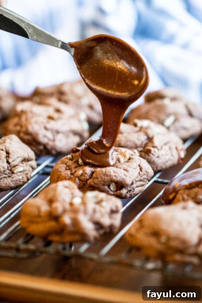 Spoon drizzling melted chocolate icing over a Texas Sheet Cake Cookie on a cooling rack, with more cookies in the background.