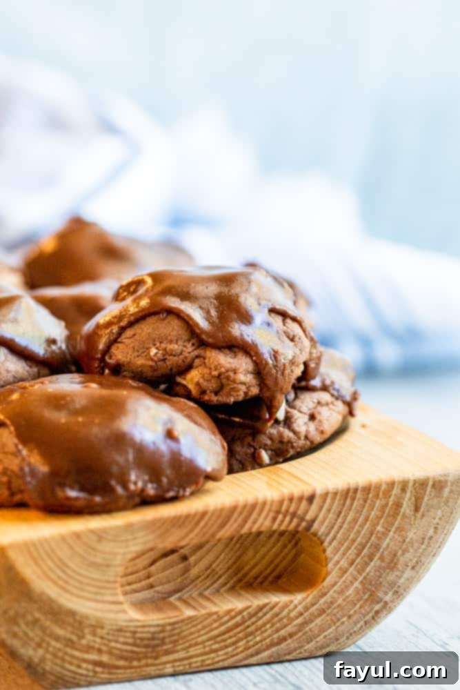 Wooden bowl holding cookies stacked on top of each other, showcasing their generous size and tempting chocolate icing.