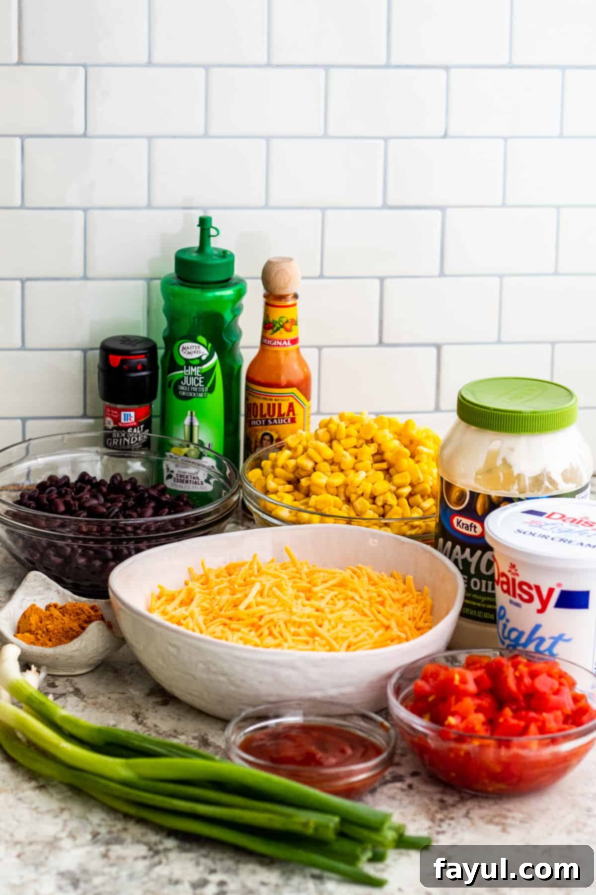 A vibrant array of Fiesta Corn Dip ingredients, including corn, beans, cheese, and sauces, neatly arranged in bowls on a white counter.