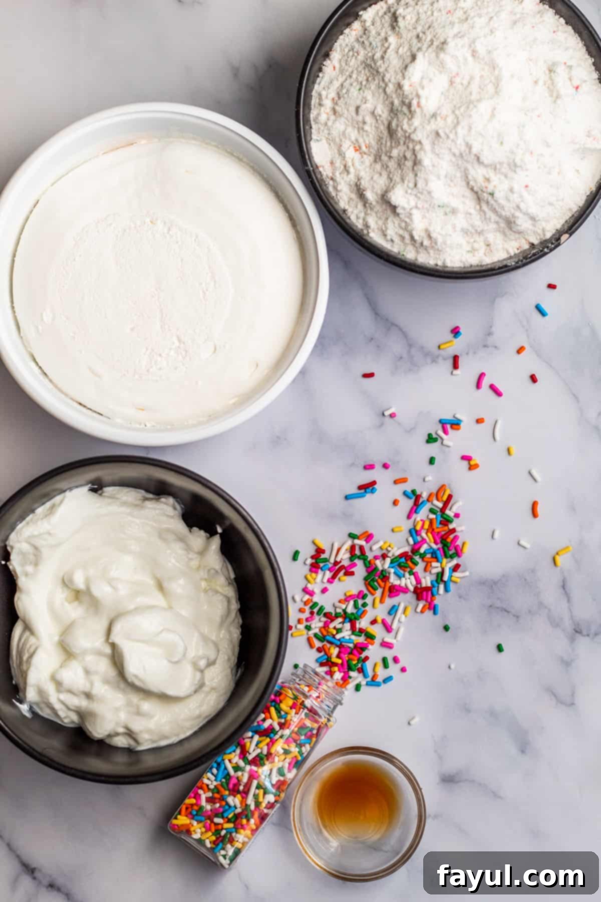 The Ultimate Funfetti Dunker Dip 3 Overhead shot of ingredients laid out on a marble table for funfetti dip including a box of cake mix, whipped topping, and Greek yogurt.