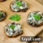 Side shot of four sweet potato slices garnished with basil leaves on a wooden cutting board.