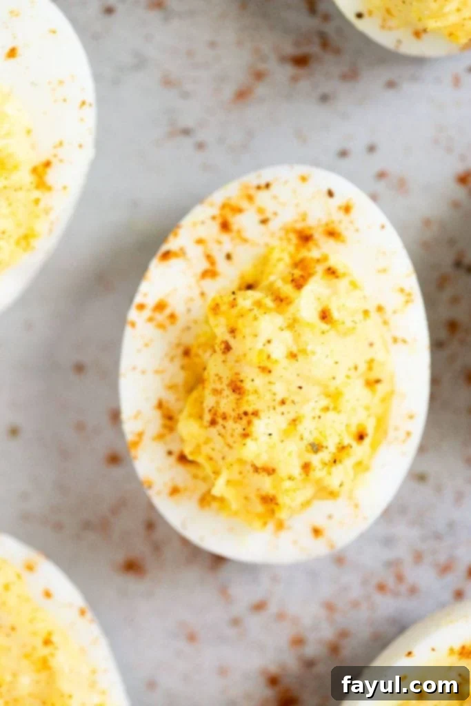 Overhead photo of a deviled egg on a white background sprinkled with paprika.