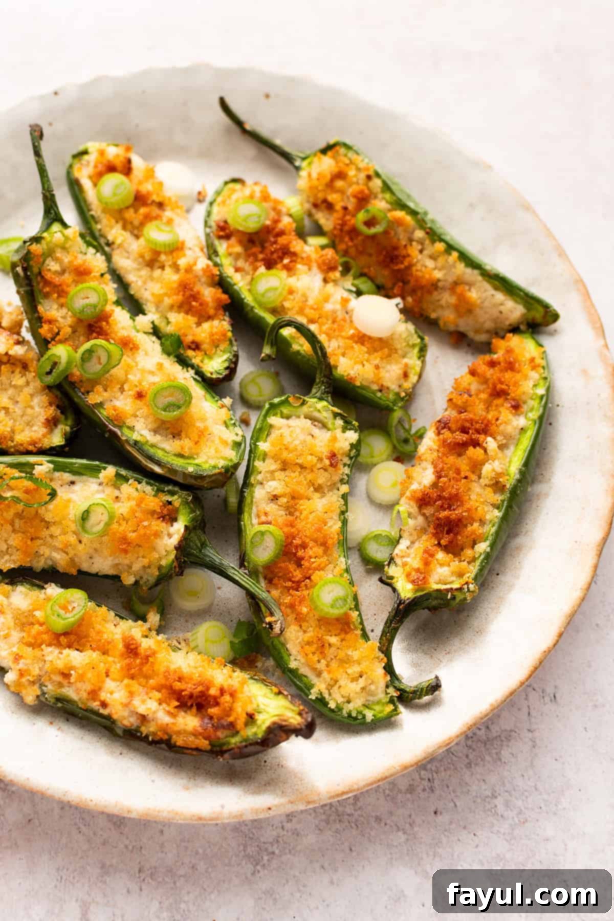 Jalapeno poppers on a round dish topped with chopped scallions.