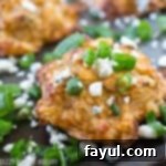Close up shot of buffalo blue cheese potato bites on a black baking sheet sprinkled with blue cheese crumbles and chives.