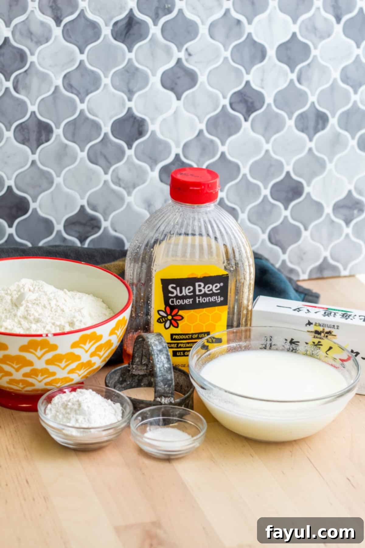Ingredients laid out on wooden table in bowls and packaging. All-purpose flour, baking powder, salt, cold butter, and buttermilk are visible, ready for baking classic Southern buttermilk biscuits.