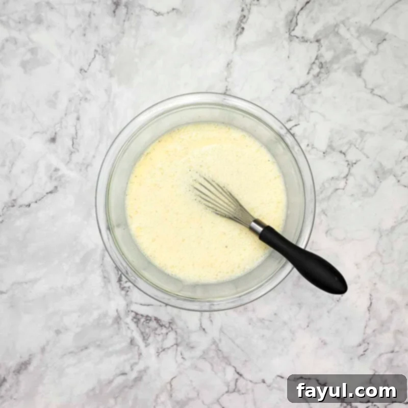 Overhead view of the first step: beating eggs, milk, and pepper together in a medium mixing bowl.