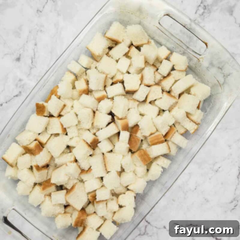 Overhead view of the second step: placing cubed bread evenly in a baking dish that has been sprayed with non-stick cooking spray.