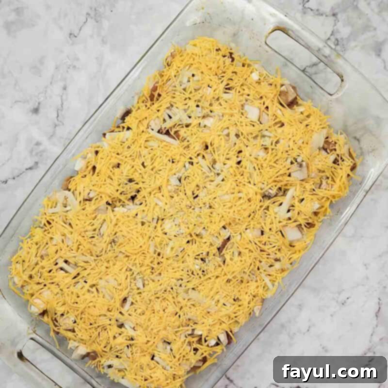 Overhead view of the final assembly step: distributing shredded cheddar cheese over the hash browns, followed by pouring the egg mixture evenly over the entire casserole before baking.