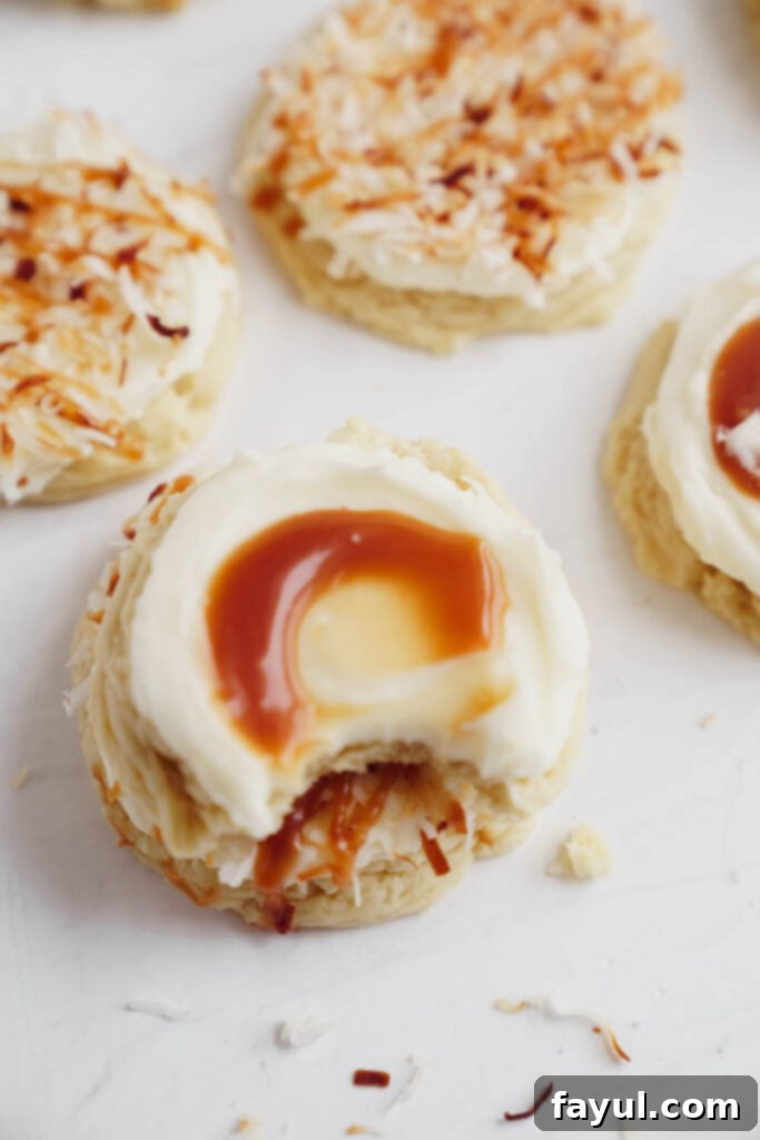 Two frosted coconut caramel sugar cookies on a white surface