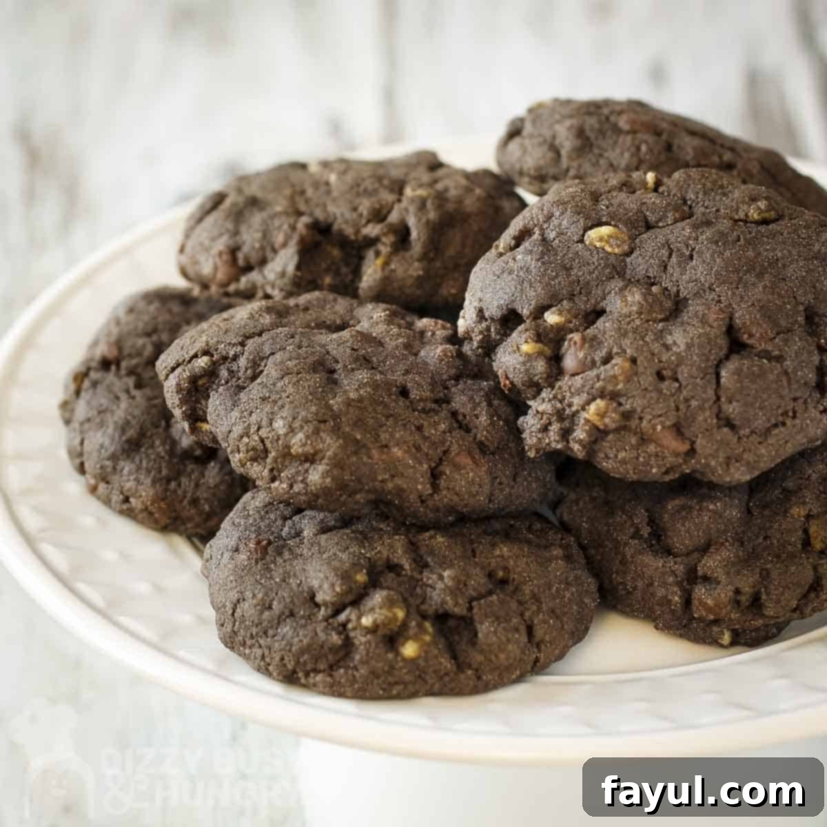 Side shot of chocolate cookies stacked on a white serving platter.
