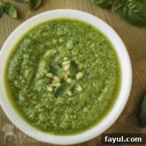 Overhead shot of broccoli pesto in a white bowl garnished with basil and pine nuts with more basil on a wooden cutting board in the background.