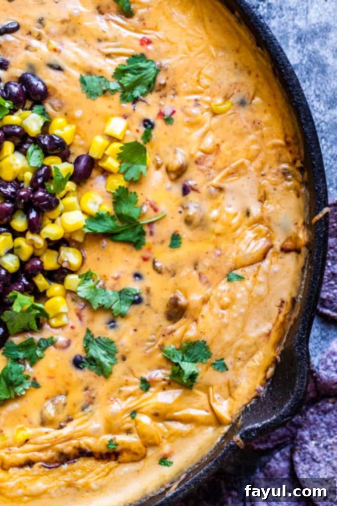 Overhead shot of creamy, loaded Cowboy Queso Dip in a black skillet on a blue counter, garnished with fresh cilantro.