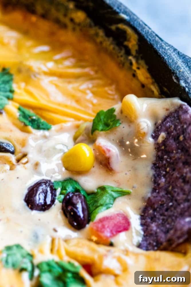 A tortilla chip being dipped into the rich, creamy Cowboy Queso Dip, showcasing its perfect consistency.