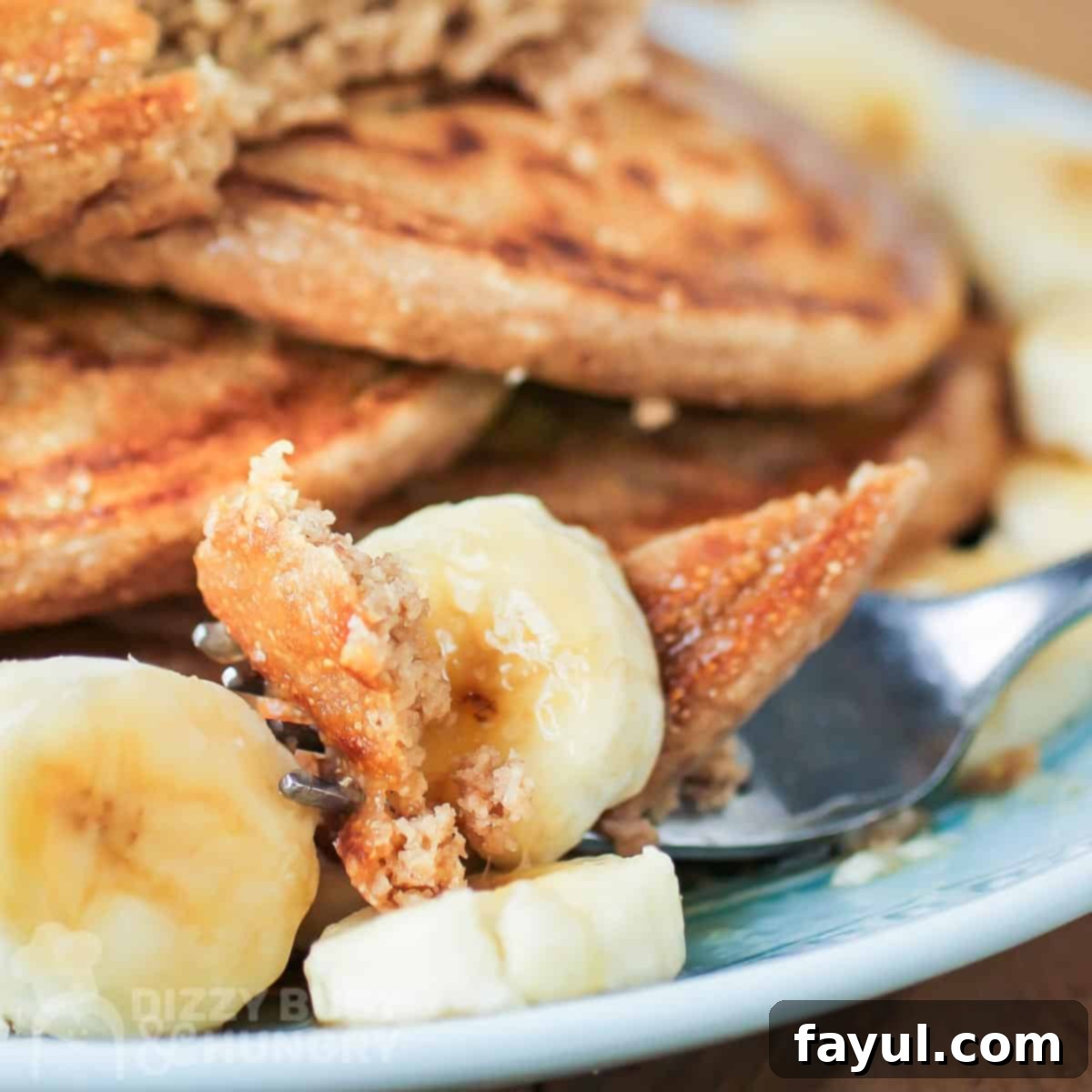 Close up side shot of a fork picking up pieces of pancake and banana on a blue plate.