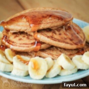 Close up side shot of multiple pancakes stacked on each other with syrup drizzled on them and bananas on the side all on a light blue plate.