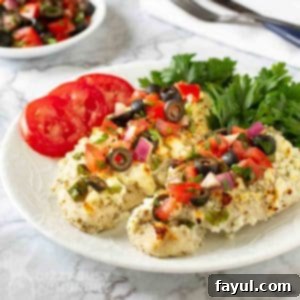 Side view of Mediterranean chicken bake with a side of sliced tomato and greens on a white plate.