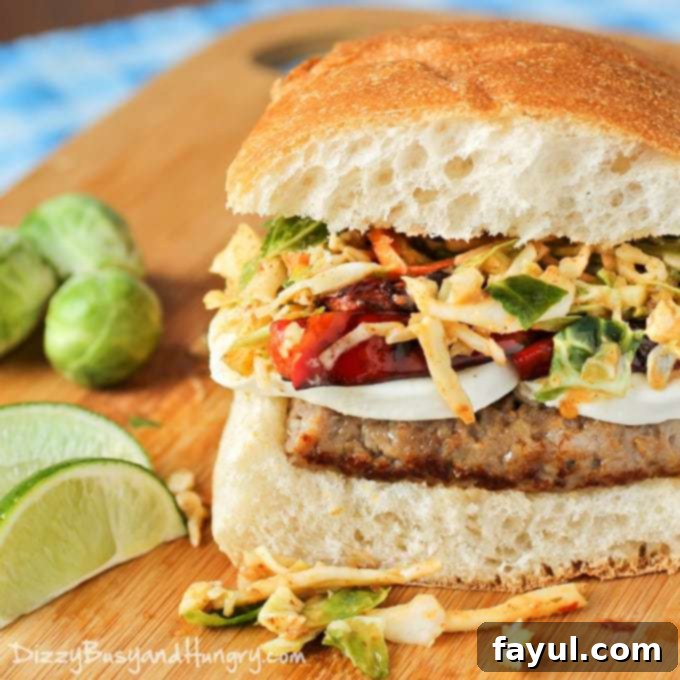 Side shot of sausage mozzarella sandwich with chipotle slaw on a wooden cutting board with sliced lime in the background.