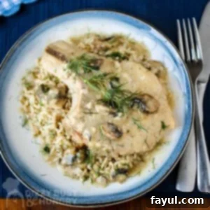 Overhead shot of a pork chop on top of mushroom soup garnished with herbs on a blue and white plate with silverware on the side on a dark blue placemat.