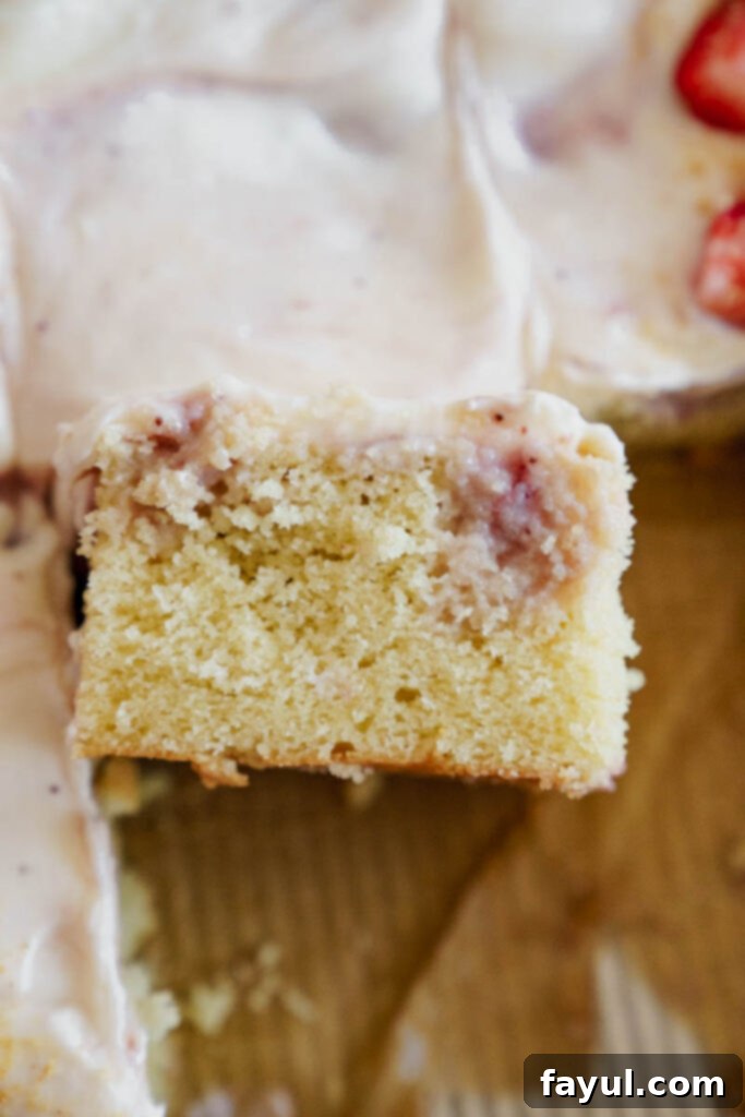 Slice of Strawberry Poke Cake showing layers of cake, strawberry sauce, and frosting