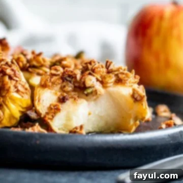 Air fryer apple half on a black plate with a bite taken out of it, garnished with a honey drizzle and a sprig of mint.
