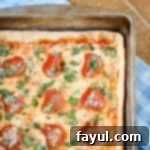 Overhead close up of a fully cooked pan pizza generously garnished with parmesan cheese and fresh basil, resting on a blue plaid cloth.
