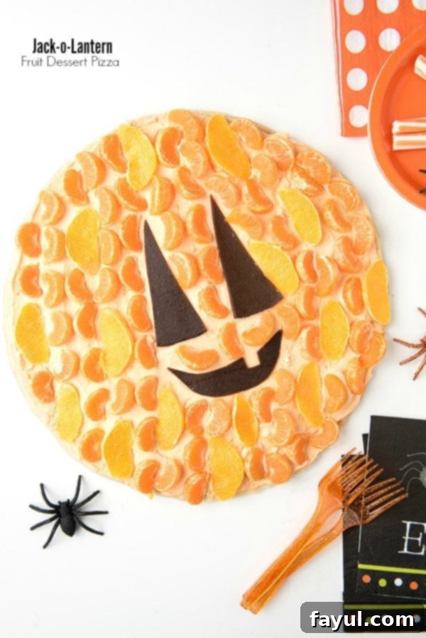 Jack-o-Lantern Fruit Dessert Pizza, decorated with colorful citrus fruits to resemble a festive Halloween pumpkin.
