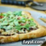 Side angled view of a whole onion bacon pizza on a gray cutting board, resting on a rustic wooden surface with a pizza cutter in the background.