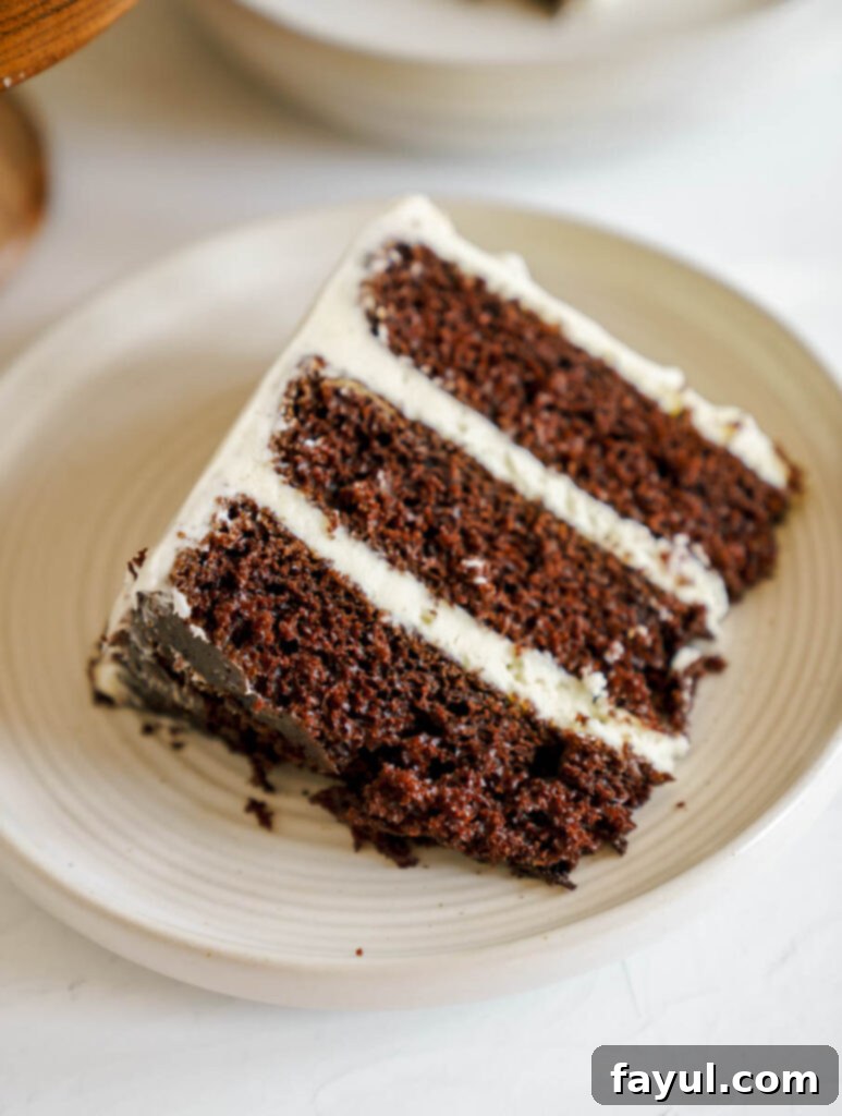 Slice of chocolate cake with cream cheese frosting on a white plate, showcasing moist layers.