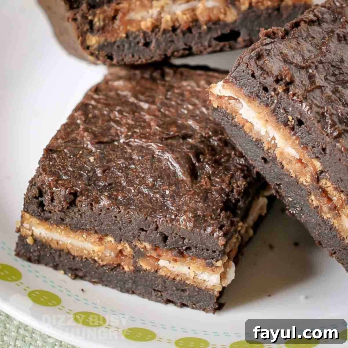 Close-up side view of three moist pumpkin brownies, with distinct Oreo layers visible, on a white plate, ready to be enjoyed.