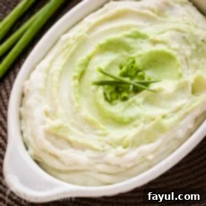 Overhead close up shot of wasabi mashed potatoes in a white baking dish garnished with green onions and chives with more green onions in the background.