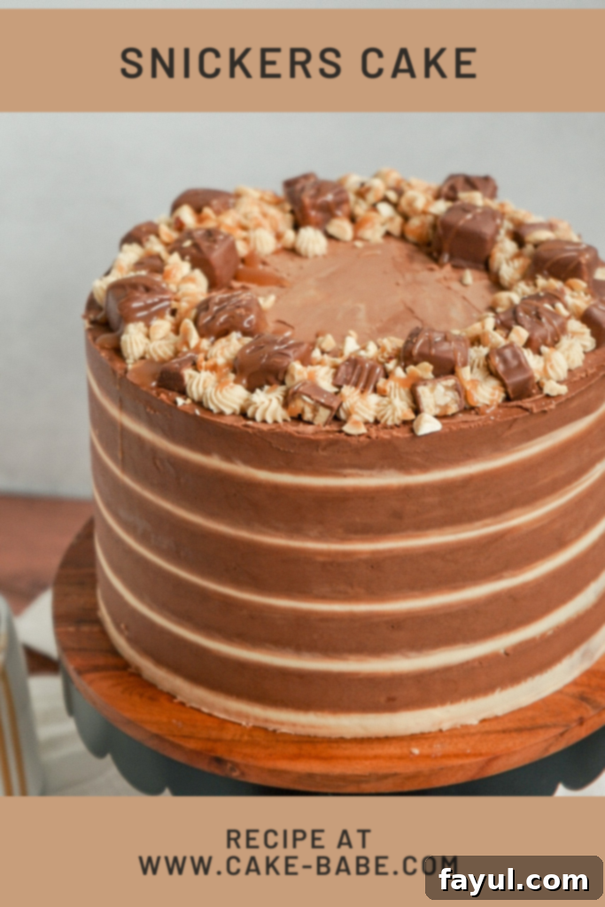 Beautifully decorated Snickers cake with chocolate and peanut butter buttercream stripes, topped with chopped Snickers bars.