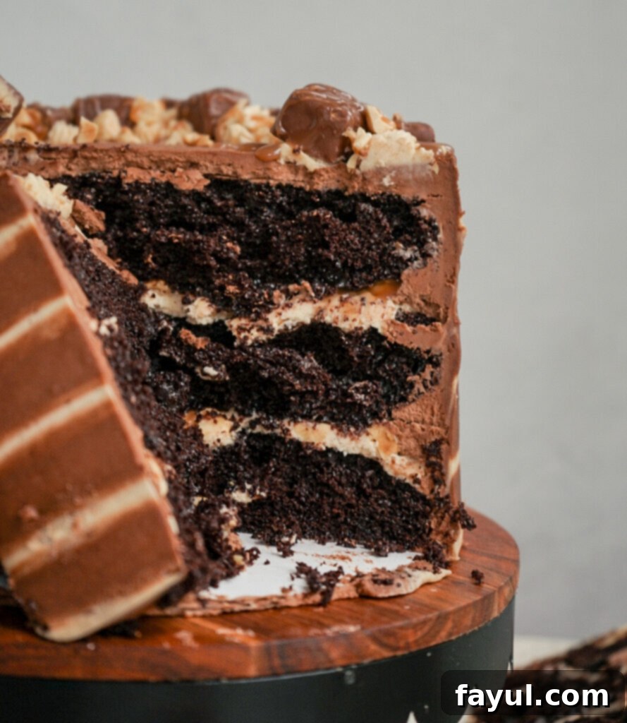 Close-up of a slice of Snickers cake, showing the distinct layers of chocolate cake, nougat, and caramel filling.