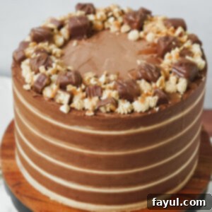 A delicious slice of Snickers cake showing all the layers of chocolate cake, nougat, caramel, and dual buttercreams.