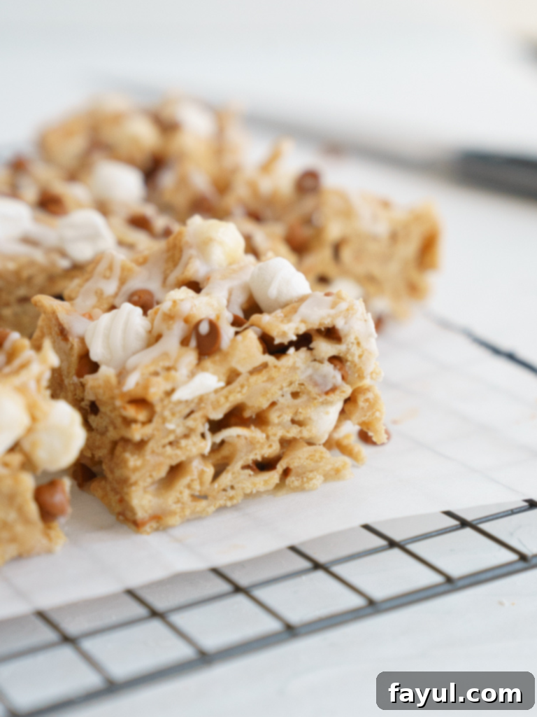 Toast Crunch Cereal Bar - A close-up of a square Cinnamon Toast Crunch Cereal Bar with a drizzle of glaze and cinnamon chips on top, set on a white surface.