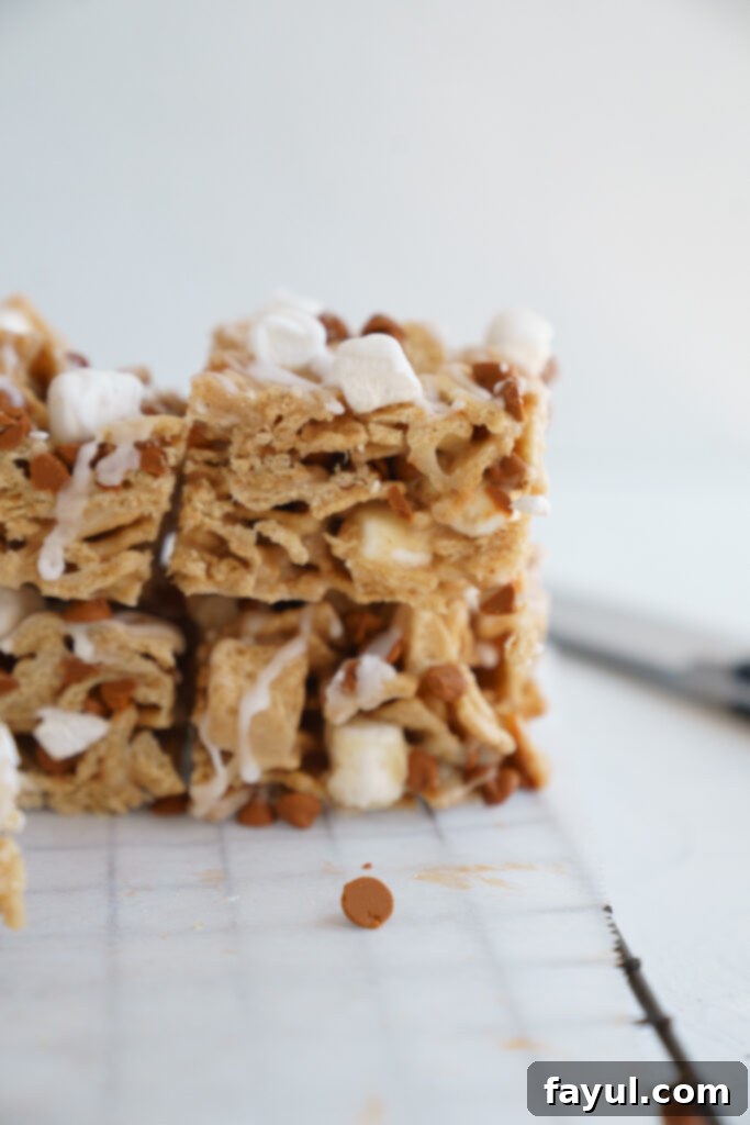 A stack of golden Cinnamon Toast Crunch Cereal Bars on a white plate, with a background of more bars and a bowl of cereal, showcasing the deliciousness of the finished product.