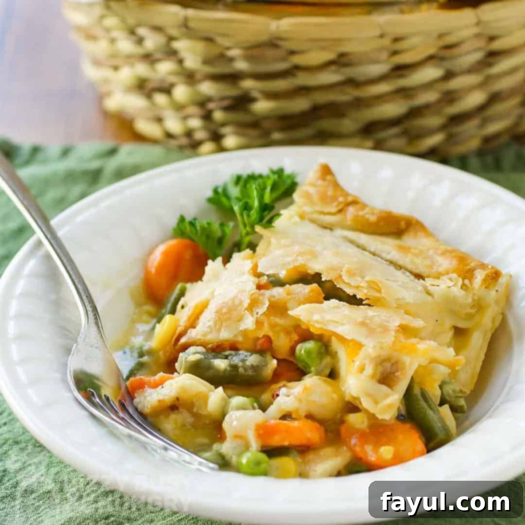 Side view of chicken pot pie in a white bowl with a fork and a green background.