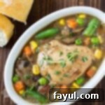 Overhead shot of crock pot Guinness chicken stew in a white oval bowl with sliced bread on the side.