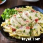 Side view of creamy crockpot chicken on penne on a black plate with herbs on the side.