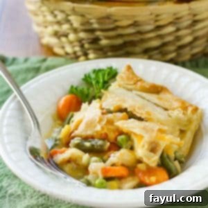 Side view of chicken pot pie in a white bowl with a fork and a green background.