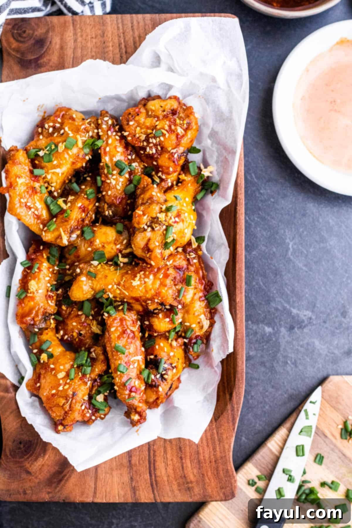 Overhead shot of pepper wings in wooden bowl on dark counter.