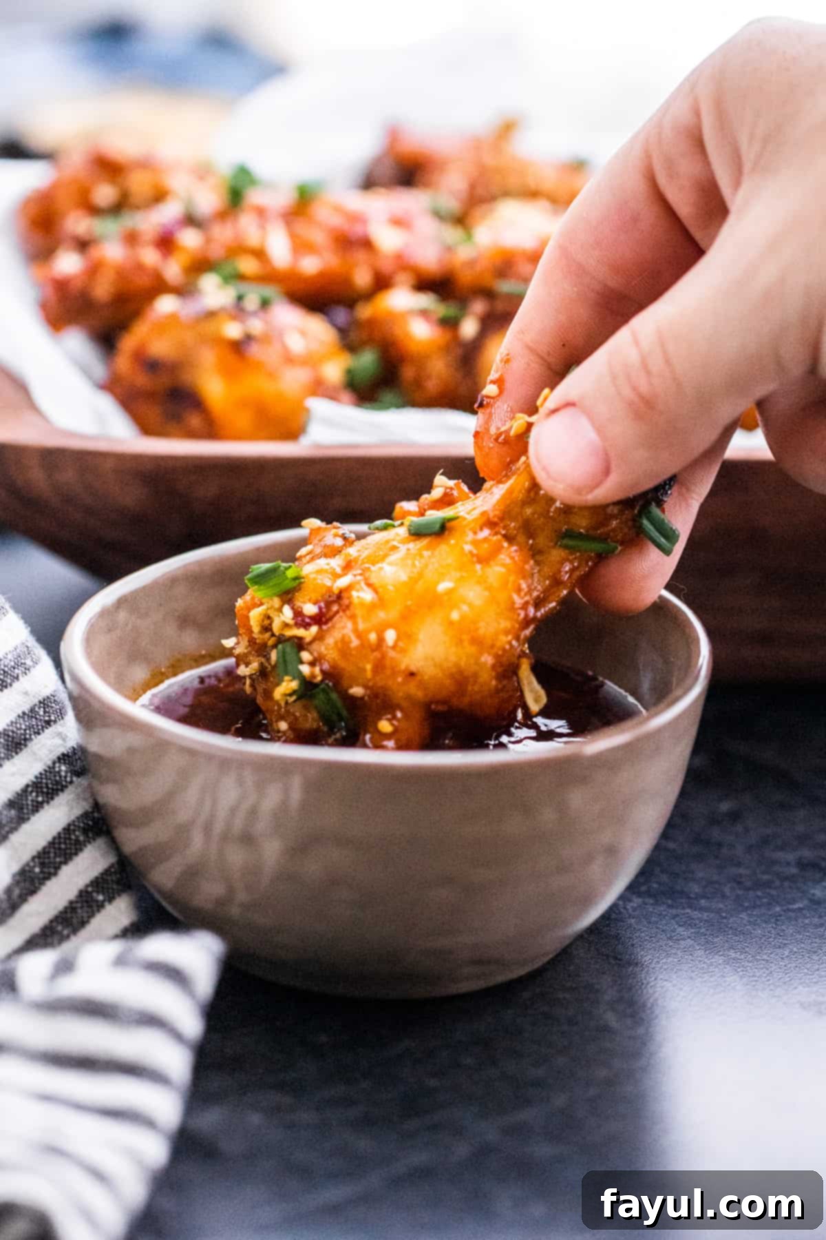 Hand dipping chicken wing into gray bowl filled with sauce.