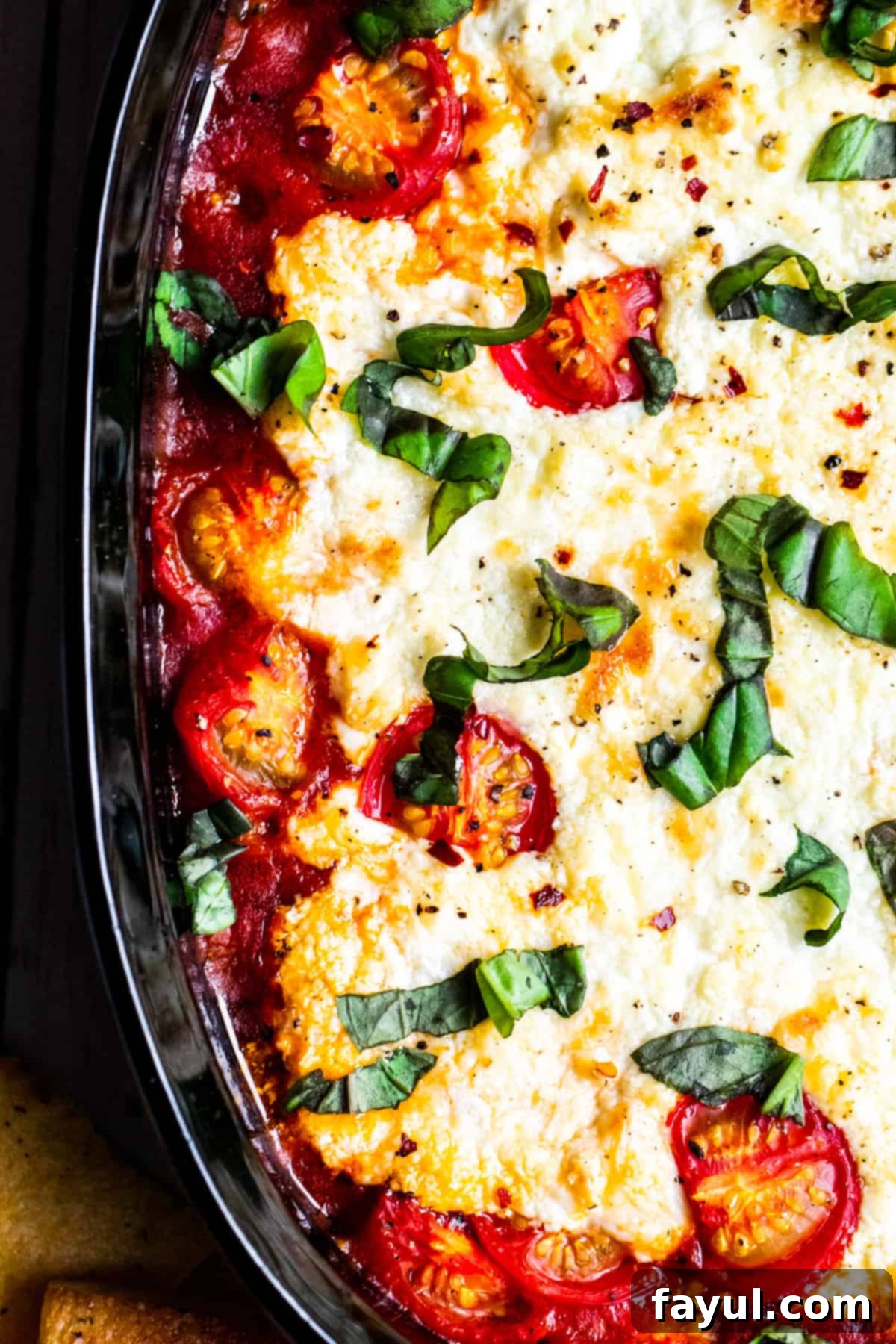 Overhead shot of goat cheese dip in black baking dish, garnished with fresh basil and red pepper flakes, ready to be served with crusty bread.